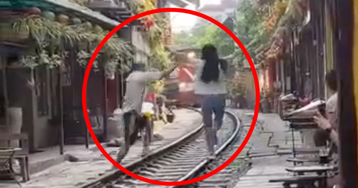 Female tourist rushes onto the train tracks as train arrives at Hanoi's train street cafe