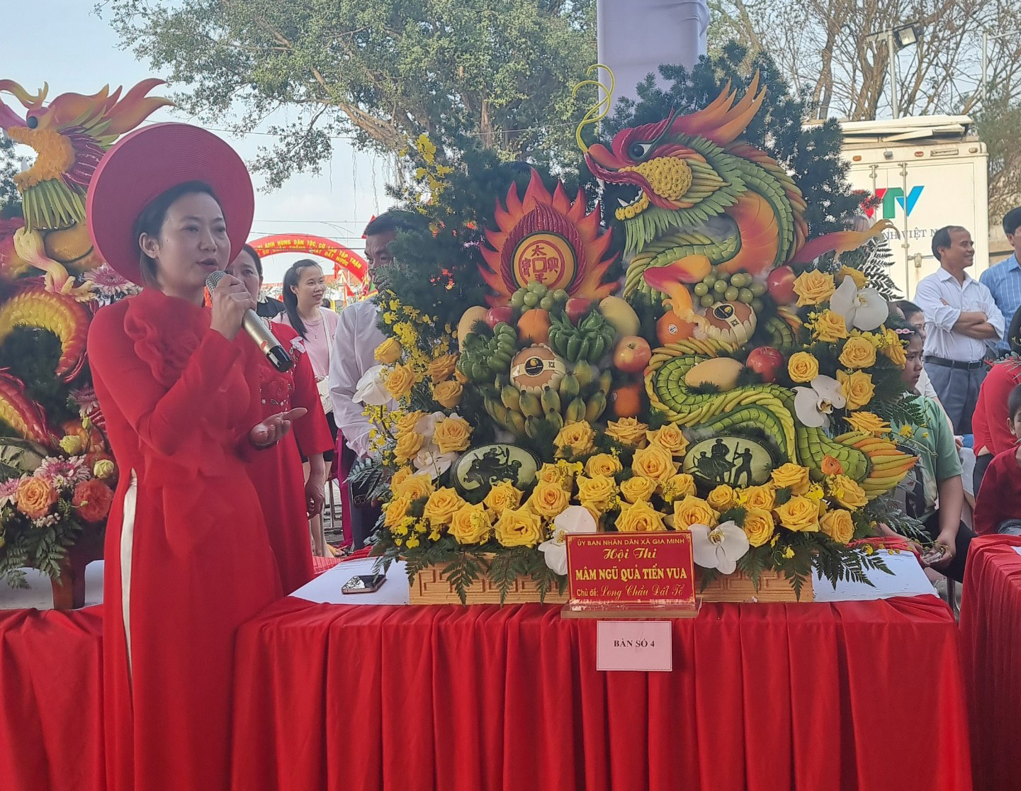A person in red dress and hat standing next to a table with flowers

Description automatically generated