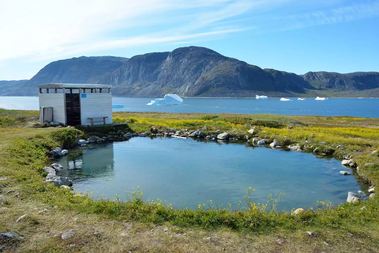 Bể nước nóng gần hồ và núi vào một ngày nắng ở Uunartoq, Greenland