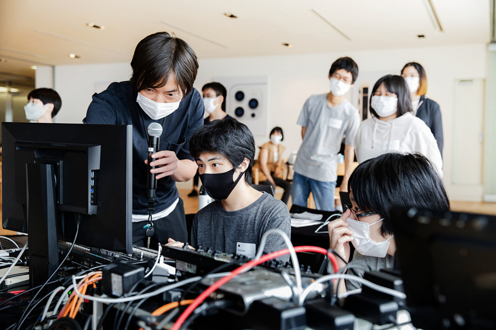 Một tình nguyện viên của Apple cầm micrô hỗ trợ chương trình Creative Studios ở Tokyo cùng với các thành viên của Sankakusha.